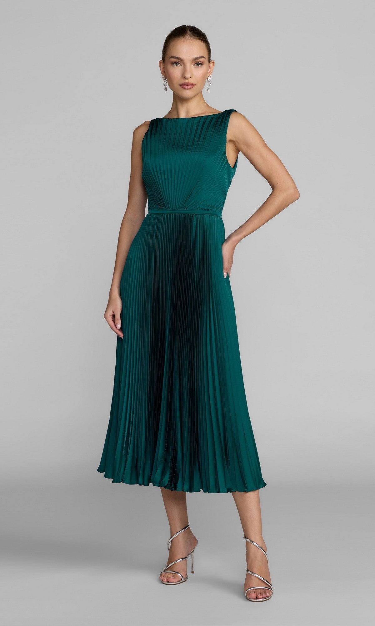 A woman wearing the Midi Party Dress: Mac Duggal 56326, a sleeveless, ocean blue pleated charmeuse dress with an elegant A-line skirt and silver strappy heels, stands against a plain gray background.